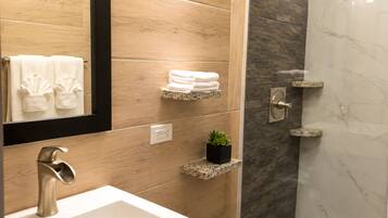 A modern bathroom with a white sink, a mirror, and a shower area.