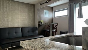 A modern kitchen with a granite countertop, a black leather sofa, and a dining area with wooden chairs. - Segovia Studio Units (Carolina)