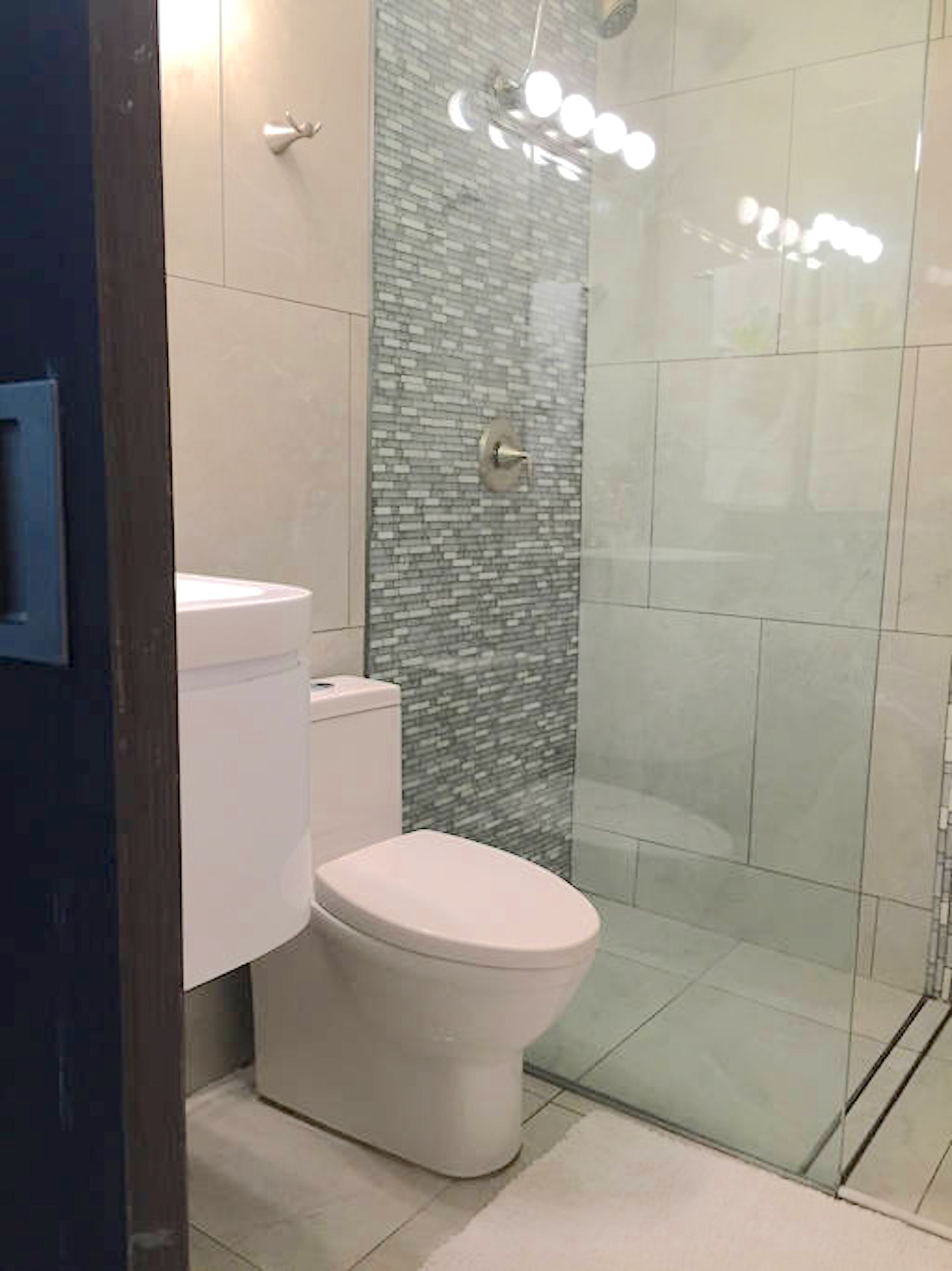 Un baño con inodoro, ducha con puerta de cristal y pared de azulejos.