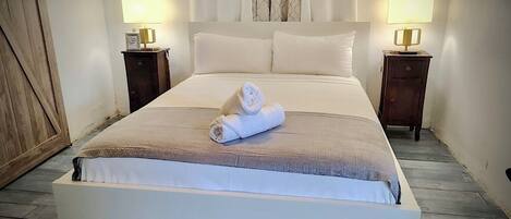 A neatly made bed with a rolled towel, two bedside tables with lamps, and a wooden wardrobe.