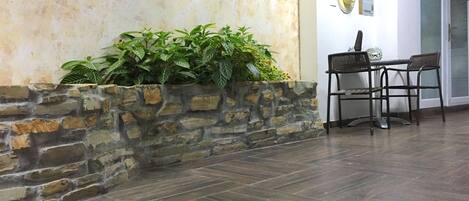 A stone planter with green plants, a wooden table with chairs, and a tiled floor.