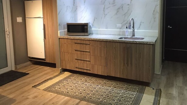 A modern kitchen with a marble backsplash, wooden cabinets, a built-in microwave, and a sink. - Segovia Studio Units (Carolina)