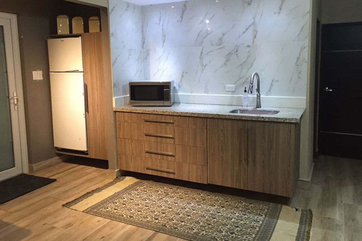 A modern kitchen with a marble backsplash, wooden cabinets, a built-in microwave, and a sink.