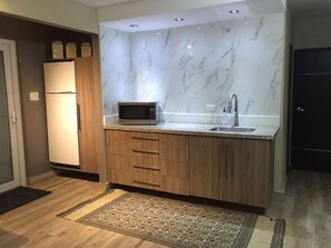 A modern kitchen with a marble backsplash, wooden cabinets, a built-in microwave, and a sink. - Segovia Studio Units (Carolina)