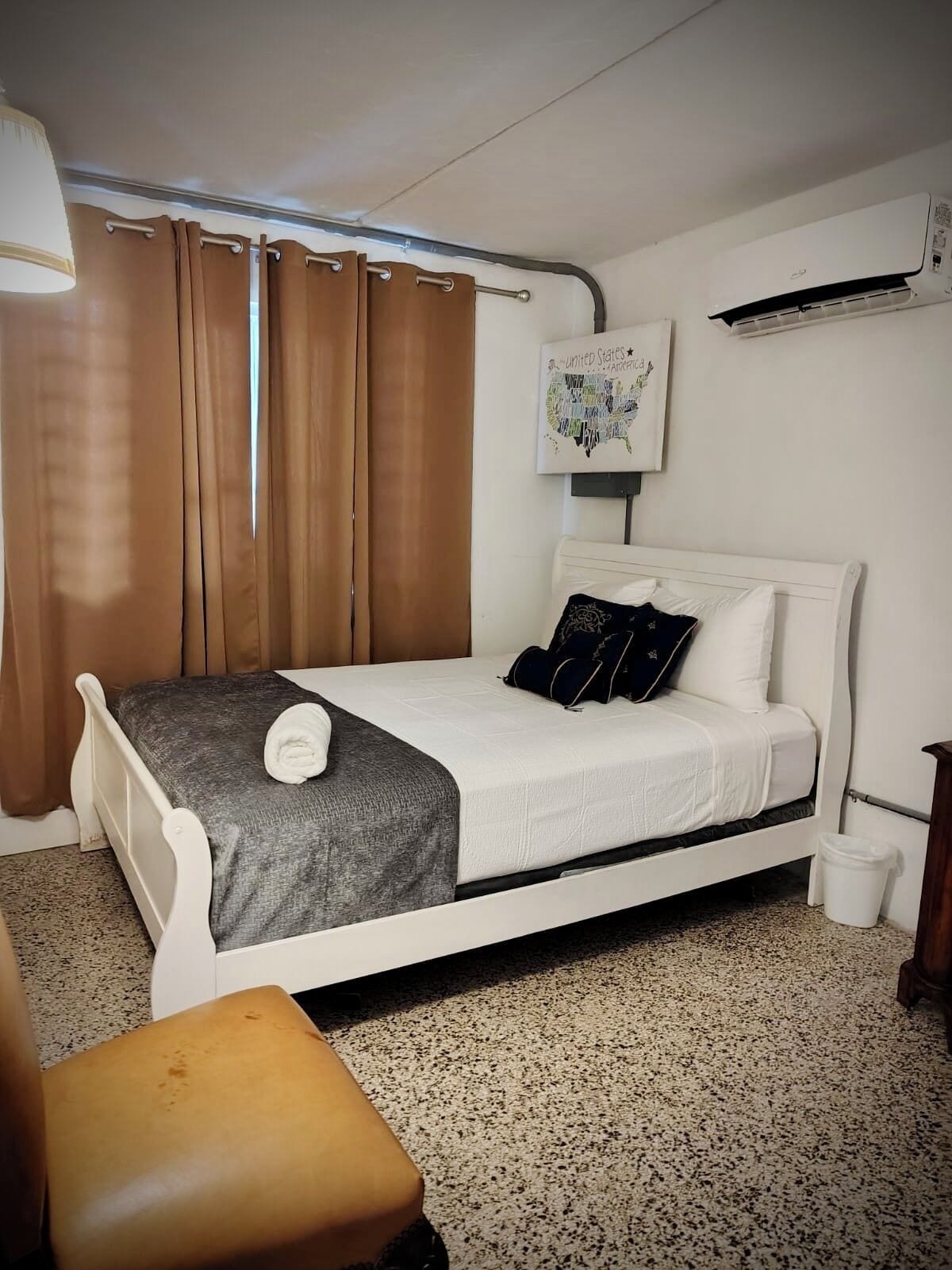 Quarto com cama, uma cadeira, ar-condicionado fixado na parede e mapa dos Estados Unidos.