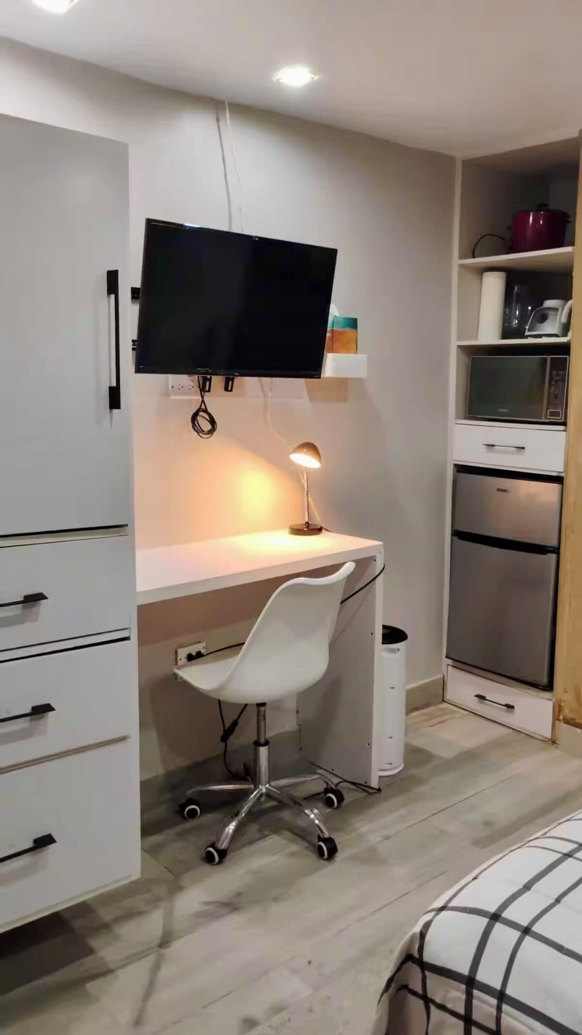 Ein gemütliches Schlafzimmer mit einem Bett, einem Schreibtisch mit Stuhl, einem Fernseher und einer kleinen Küchenzeile.