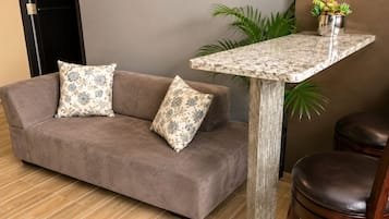 A room with a brown sofa, two patterned pillows, a wooden table, a potted plant, and a leather chair.
