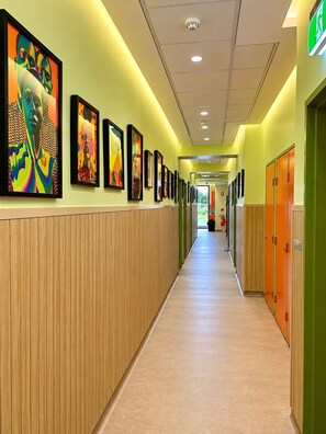 A hallway with framed artwork on the walls, wooden paneling, and a carpeted floor. - Breeze Lodge - Hostel (Kangaroo Point)