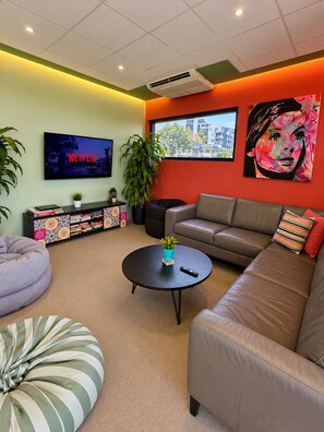 A modern living room with a sofa, a coffee table, a bean bag, a TV, and a bookshelf. - Breeze Lodge - Hostel (Kangaroo Point)