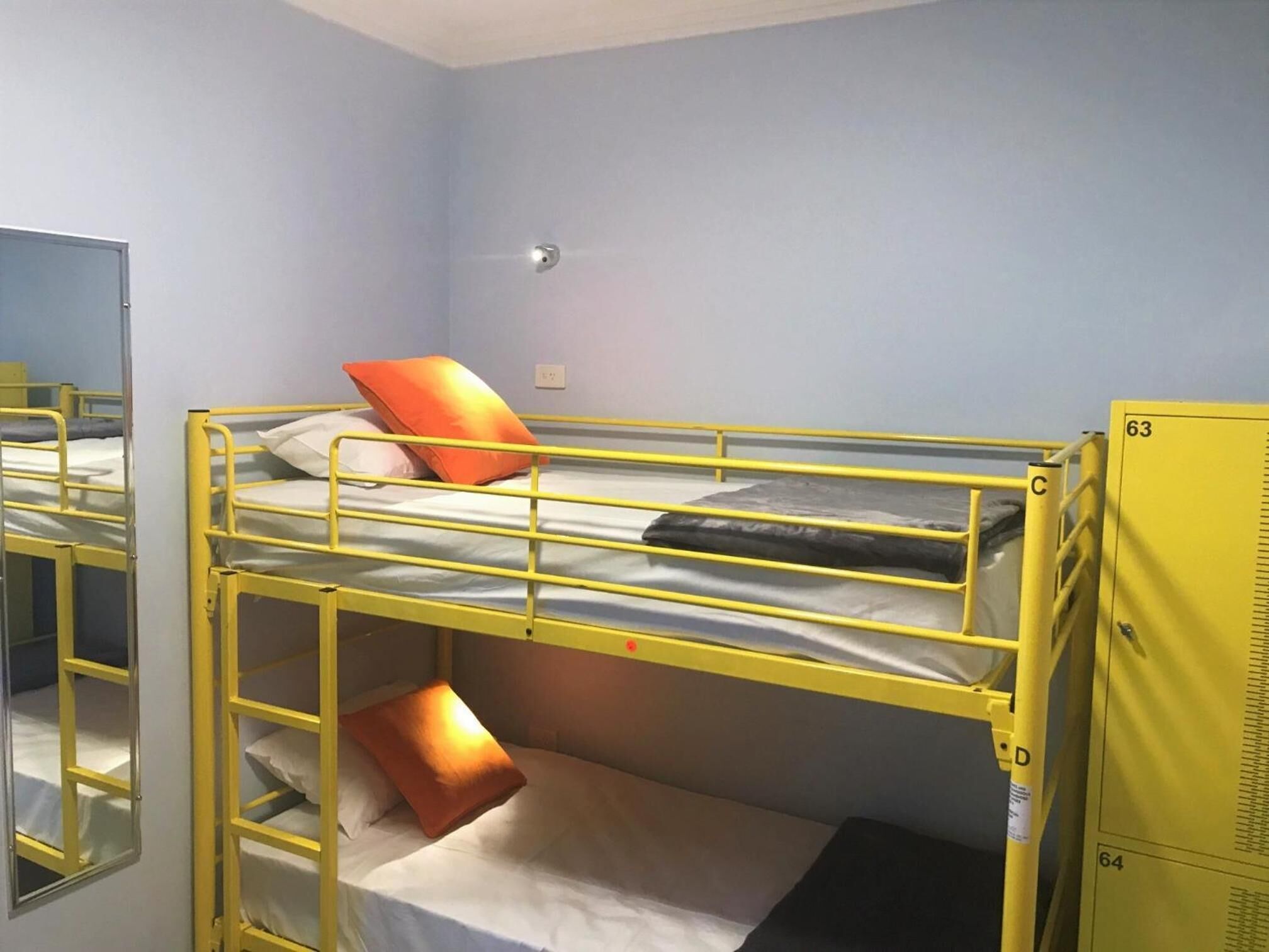 A bunk bed room with a mirror, a light switch, and a yellow storage cabinet.