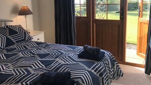 A bedroom with a large bed, a nightstand, a lamp, and a view of the garden through an open door. - Lakeside Cottage In Kesh with panoramic views over Lough Erne,  (Kesh, Fermanagh)