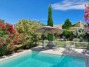A swimming pool with a white fence, surrounded by lush greenery and flowering plants.