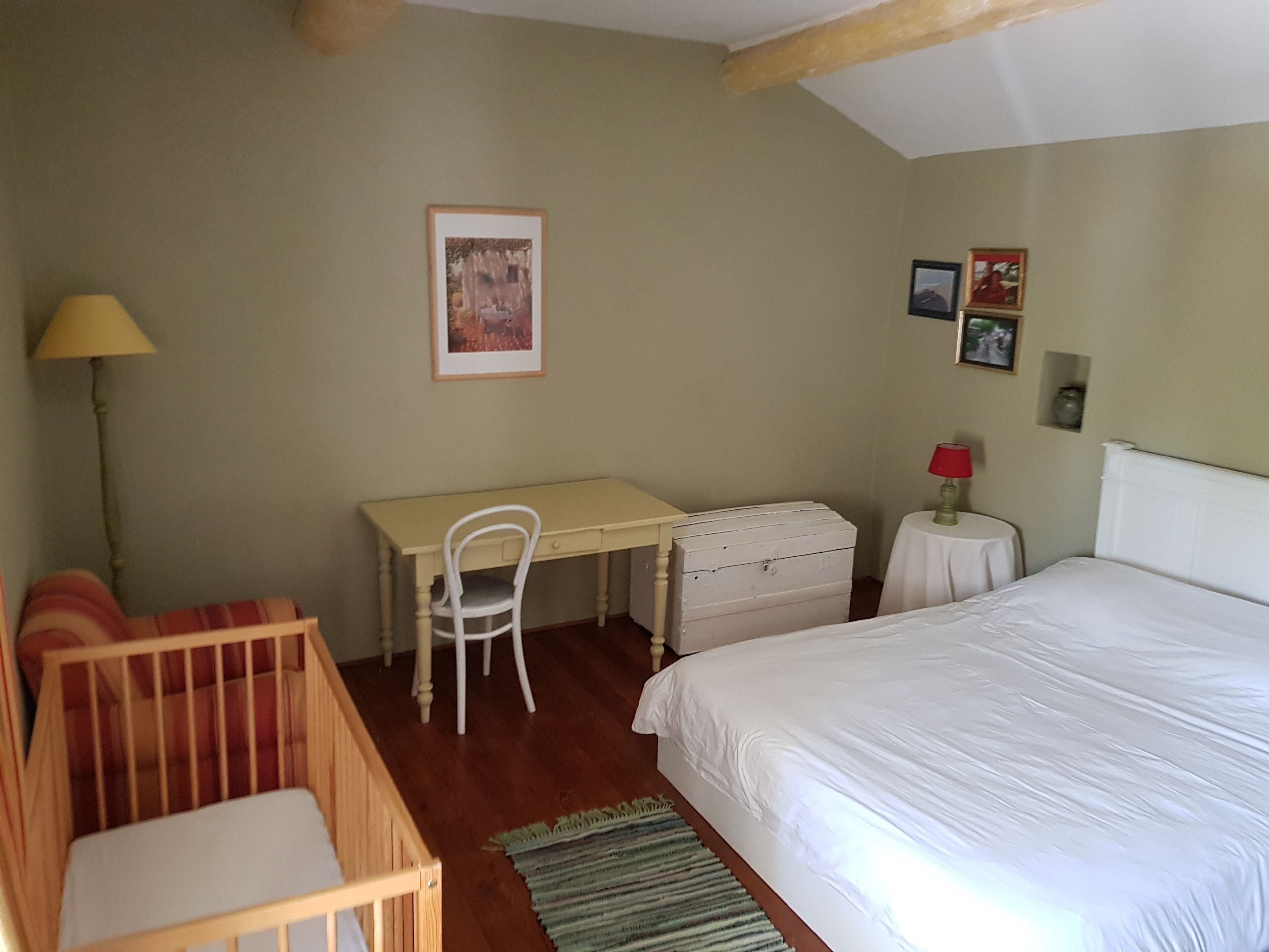 Une chambre à coucher comprenant un lit, un bureau, une chaise, un berceau et une lampe.