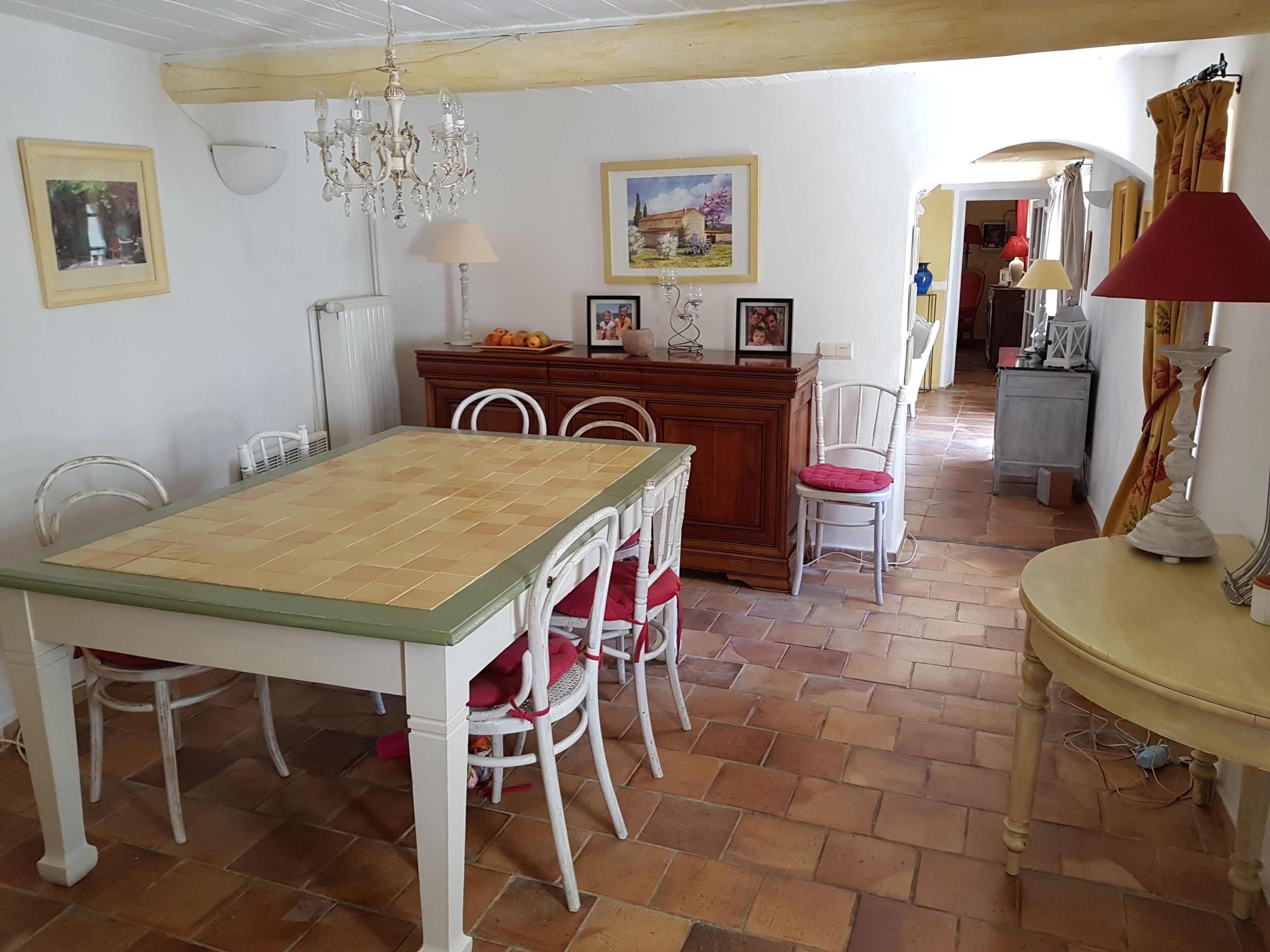 A dining area with a wooden table and chairs, a chandelier, and a cabinet with framed pictures.