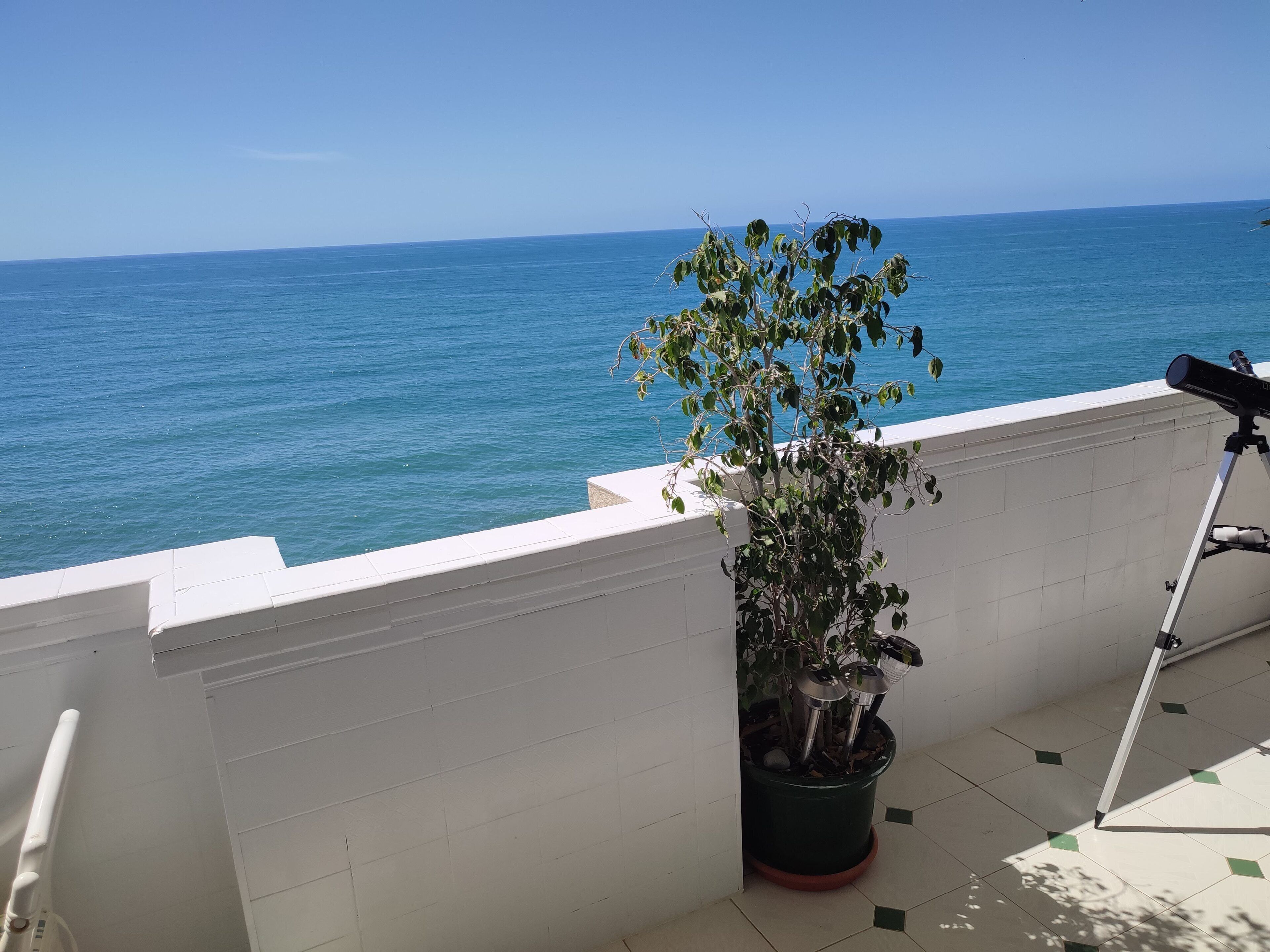 A balcony with a potted plant, a telescope, and a view of the sea.
