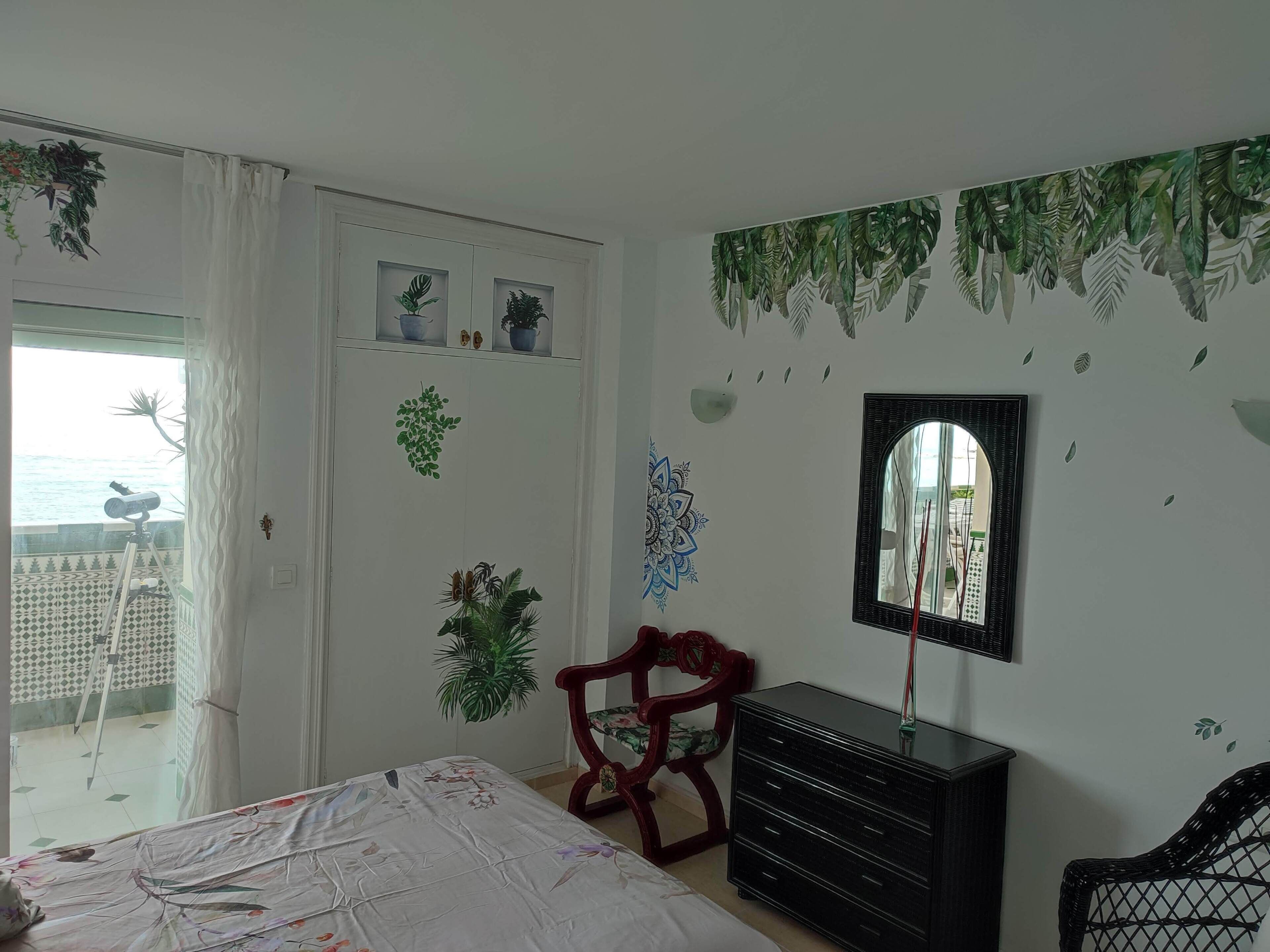 Une chambre à coucher avec un lit, une commode, une chaise, un miroir et une fenêtre avec des rideaux.