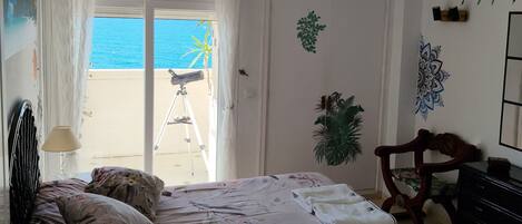 Une chambre à coucher avec un lit, un bureau, une chaise, une armoire et une vue sur la mer.