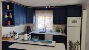 A compact kitchen with dark blue cabinets, a white refrigerator, and a window with a curtain. - Apartment on the semi-private beach, terrace with sea views and WIFI (Benalmádena)