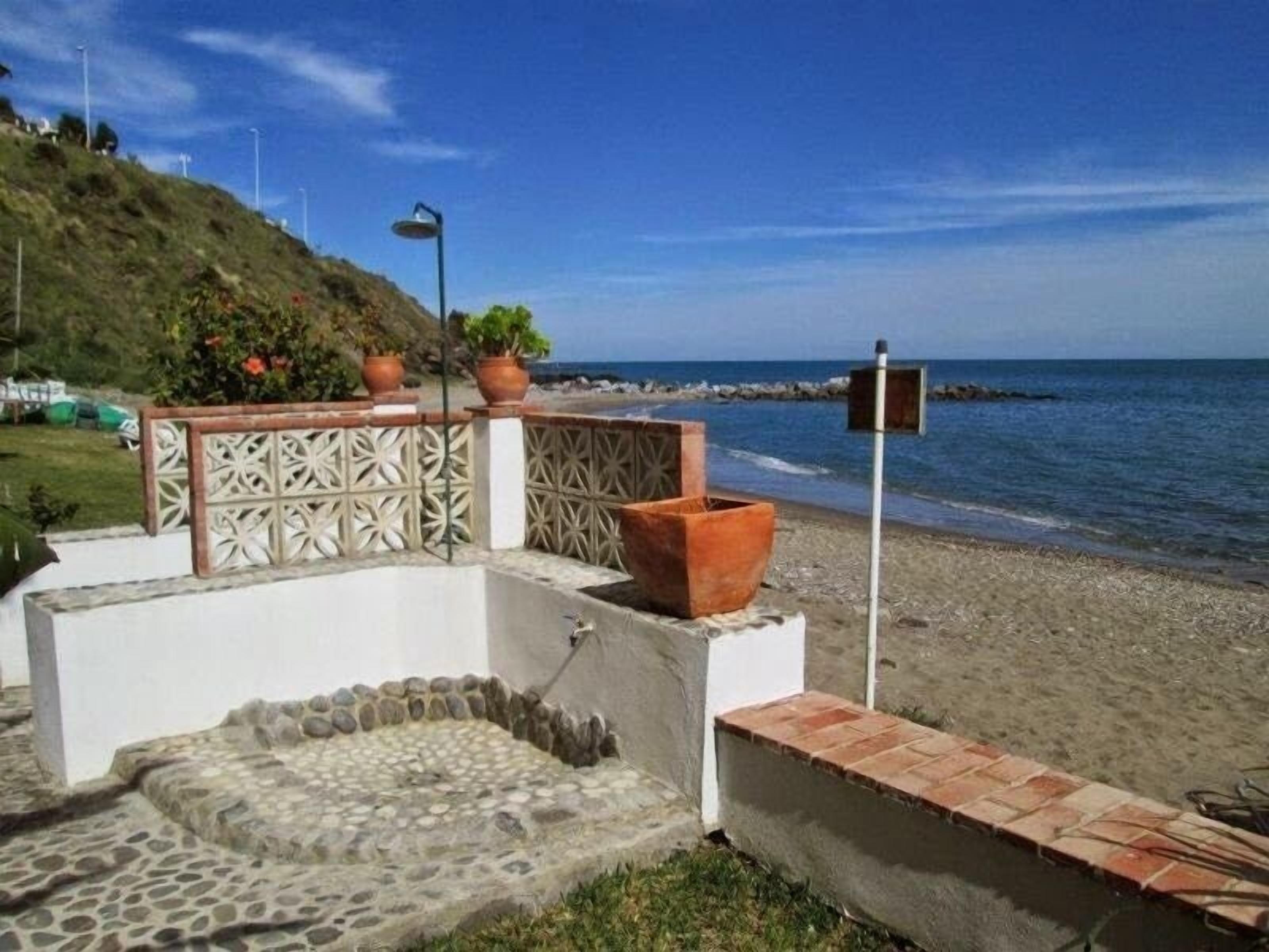 A beachside patio with a stone fountain, terracotta pots, and a view of the ocean.
