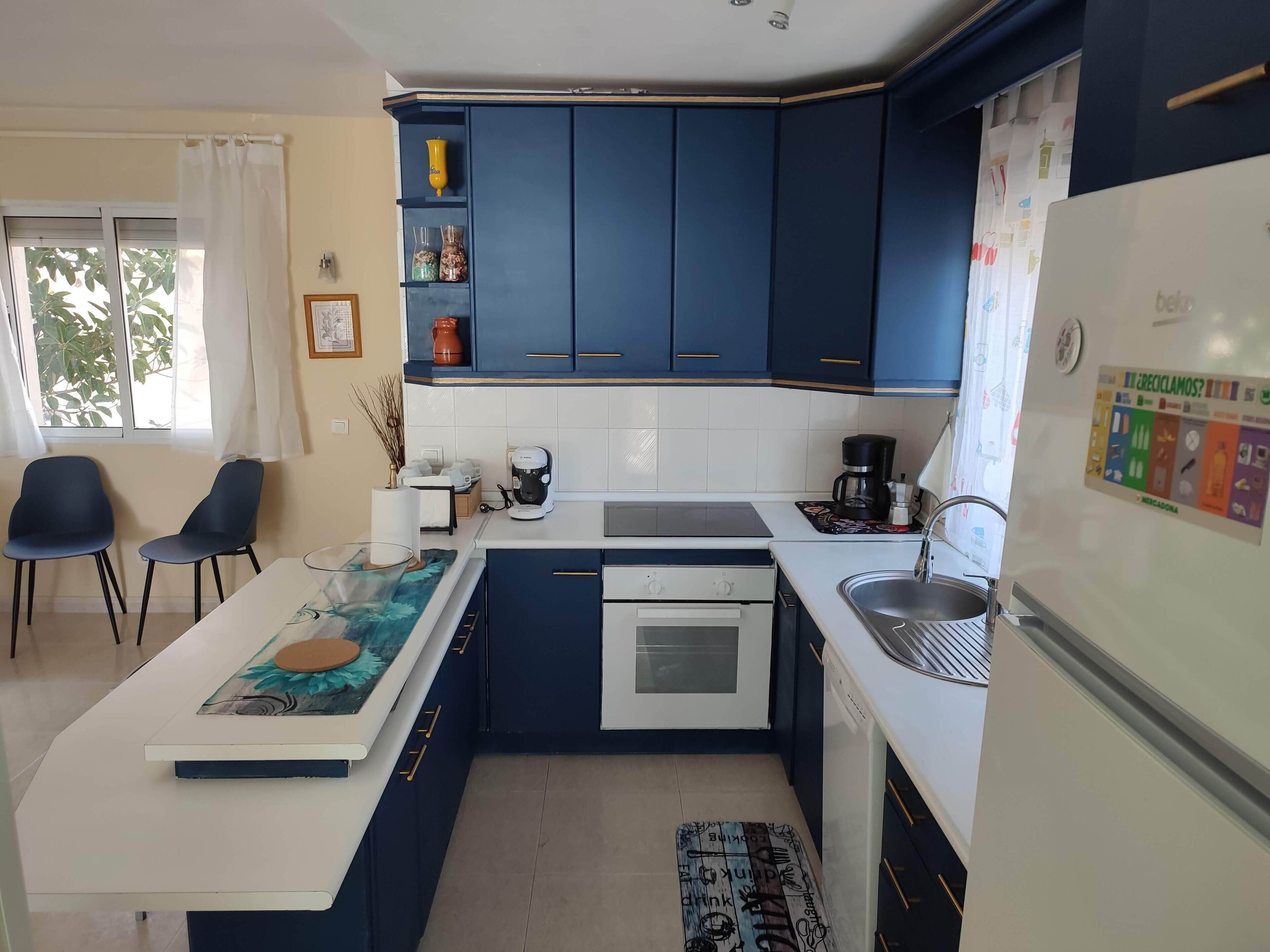 Een moderne keuken met blauwe kastjes, een witte aanrecht en een koffiezetapparaat, plus een spoelbak.