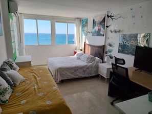 Un dormitorio con cama, escritorio, silla, televisor y vista al mar.