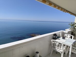 Un balcon avec vue sur la mer, des meubles d’extérieur blancs et un sol carrelé.