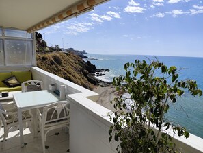 Un balcón con vista al océano, una mesa blanca, una silla blanca y un sofá verde.