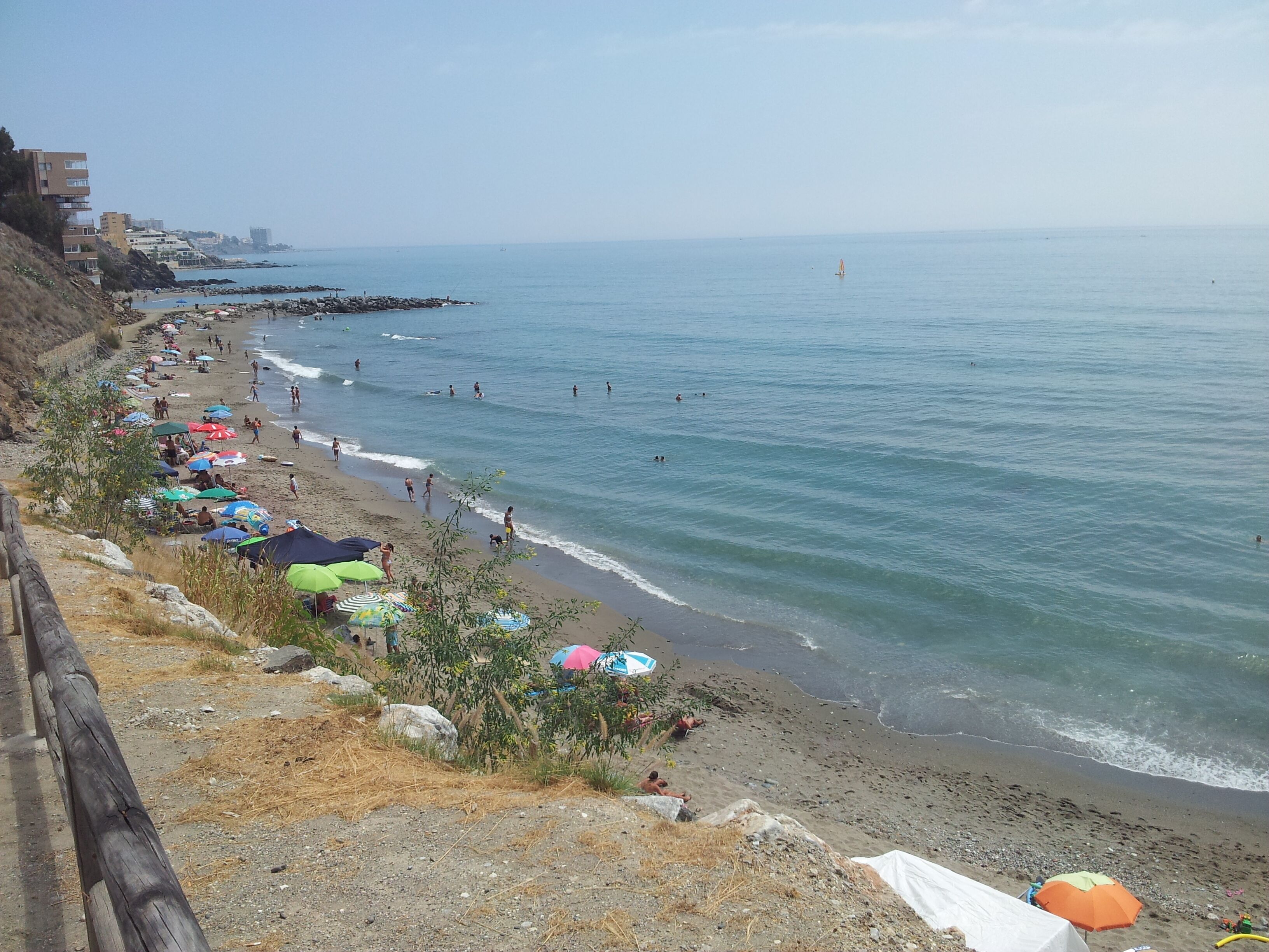 Een strand met parasols en mensen.