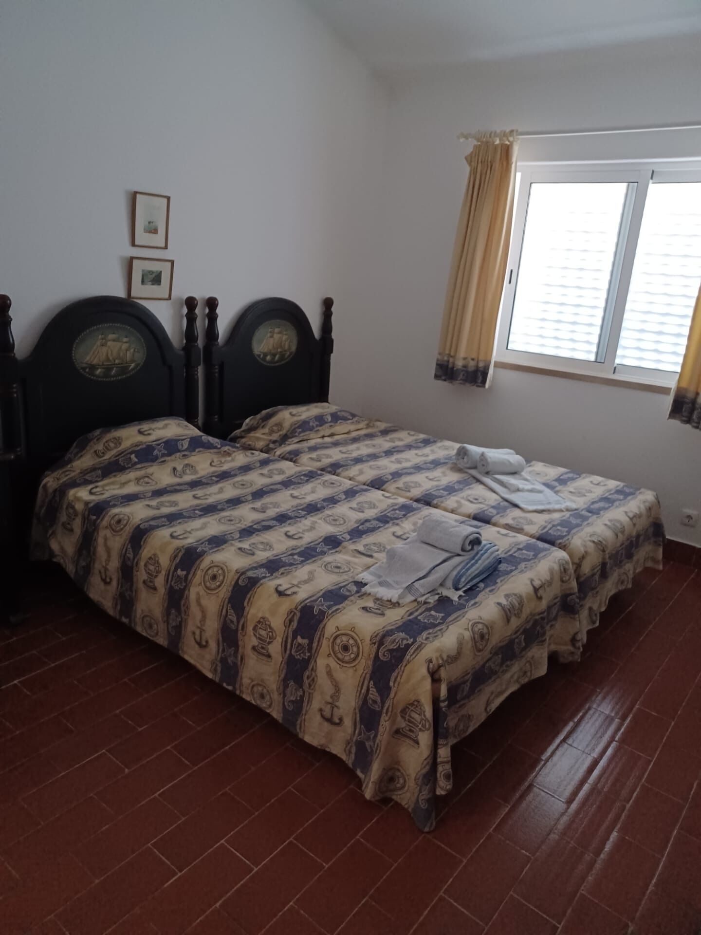 Une chambre avec un lit double, une fenêtre avec des rideaux et un sol carrelé.
