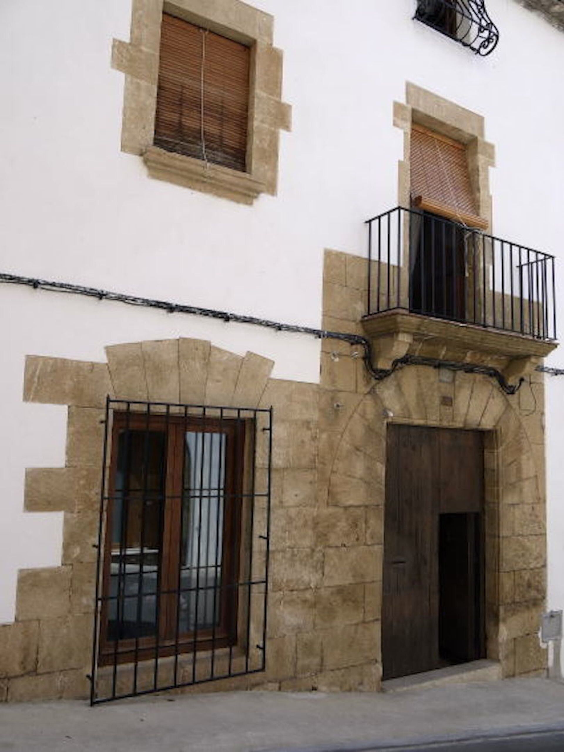A building with a stone facade, a wooden door, and a balcony with a metal railing.