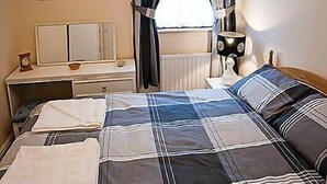 A bedroom with a bed, a dresser, a mirror, a lamp, and a window with curtains. - Superb sea views and  great location (Looe)