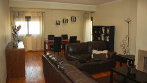 A living room with a brown leather sofa, a dining table with chairs, a bookshelf, and a fireplace.