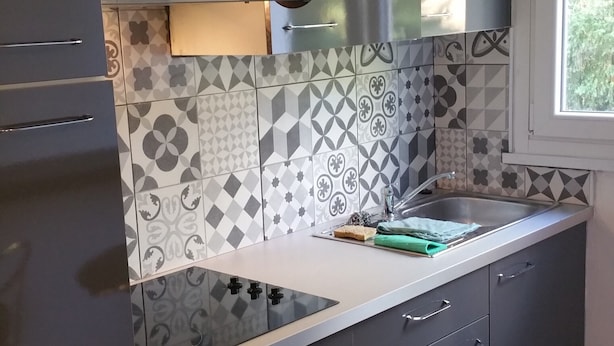 A modern kitchen with grey cabinets, a stainless steel range hood, patterned backsplash, and a window providing natural light. - Apartment for 1 to 4 people on the road of the castles (Meung-sur-Loire)