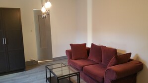A living room with a dark wooden wardrobe, a glass coffee table, and a red sofa with matching cushions. - Apartment for 1 to 4 people on the road of the castles (Meung-sur-Loire)