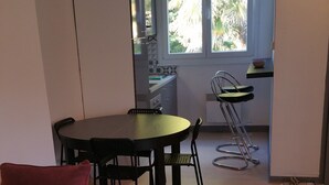 A living room with a red sofa, a glass-top coffee table, and a dining area with a table and chairs. There is a kitchen in the background with a window and a bowl on a shelf. - Apartment for 1 to 4 people on the road of the castles (Meung-sur-Loire)