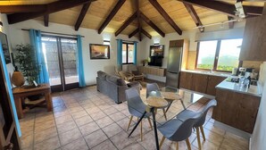 A spacious living area with a high ceiling, a dining table with chairs, a sofa, and a kitchen area with a refrigerator and sink. - Spacious villa in Lajares with separate relaxation area and garden. (Lajares)