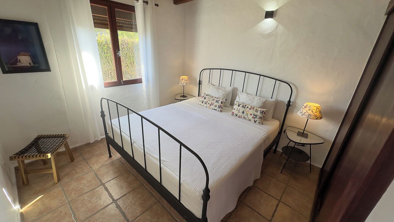 A bedroom with a bed, bedside tables, a small stool, and a window with curtains.