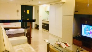 Une chambre d’hôtel avec un lit, un canapé, une table en verre avec des magazines, une télévision et un coin cuisine à l’arrière-plan.
