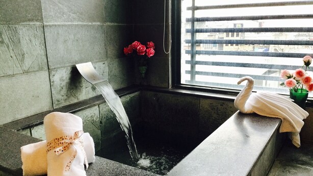 Une salle de bain avec une baignoire, un porte-serviettes et une fenêtre donnant sur des immeubles.