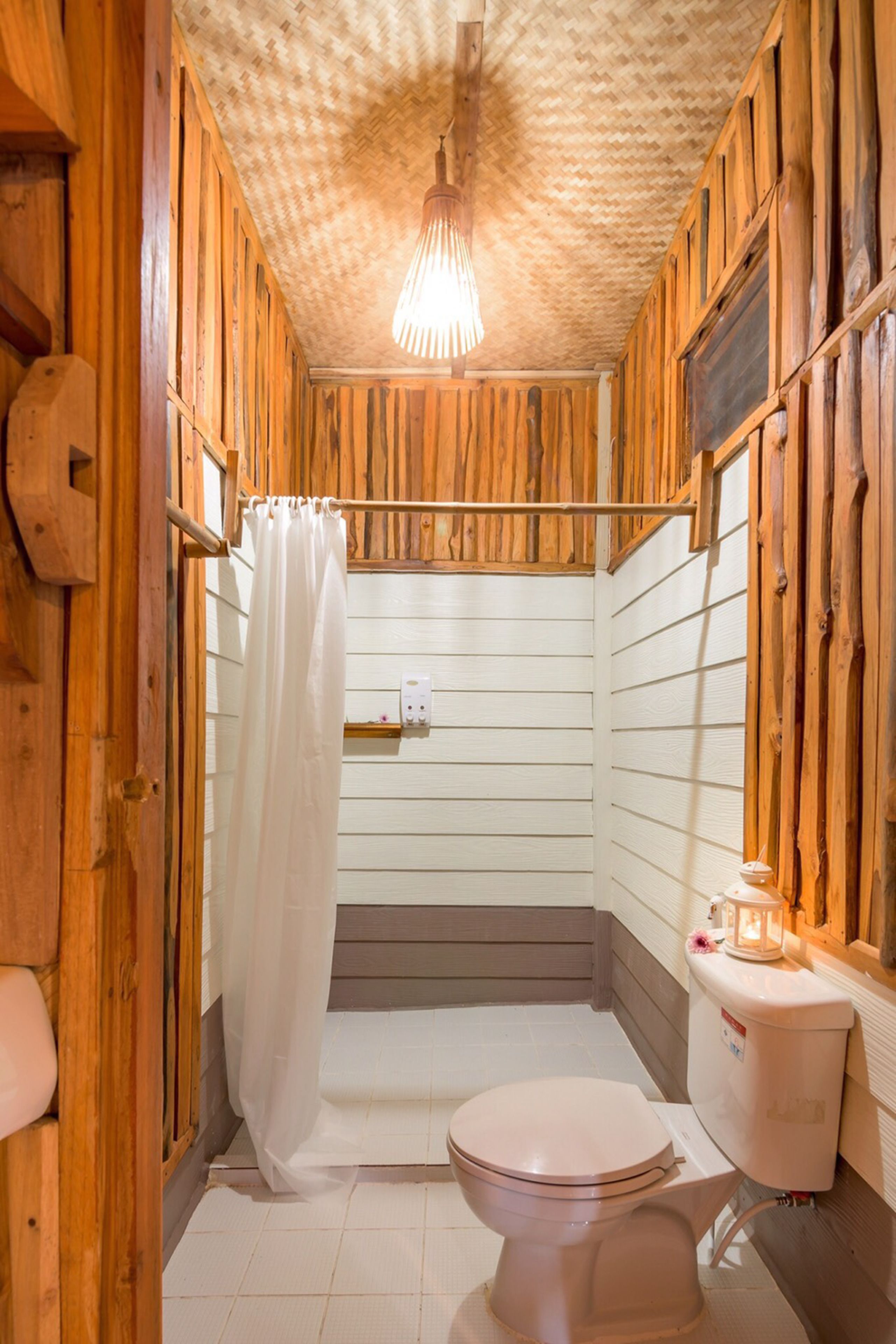 A wooden bathroom with a toilet, a shower curtain, and a hanging light fixture.