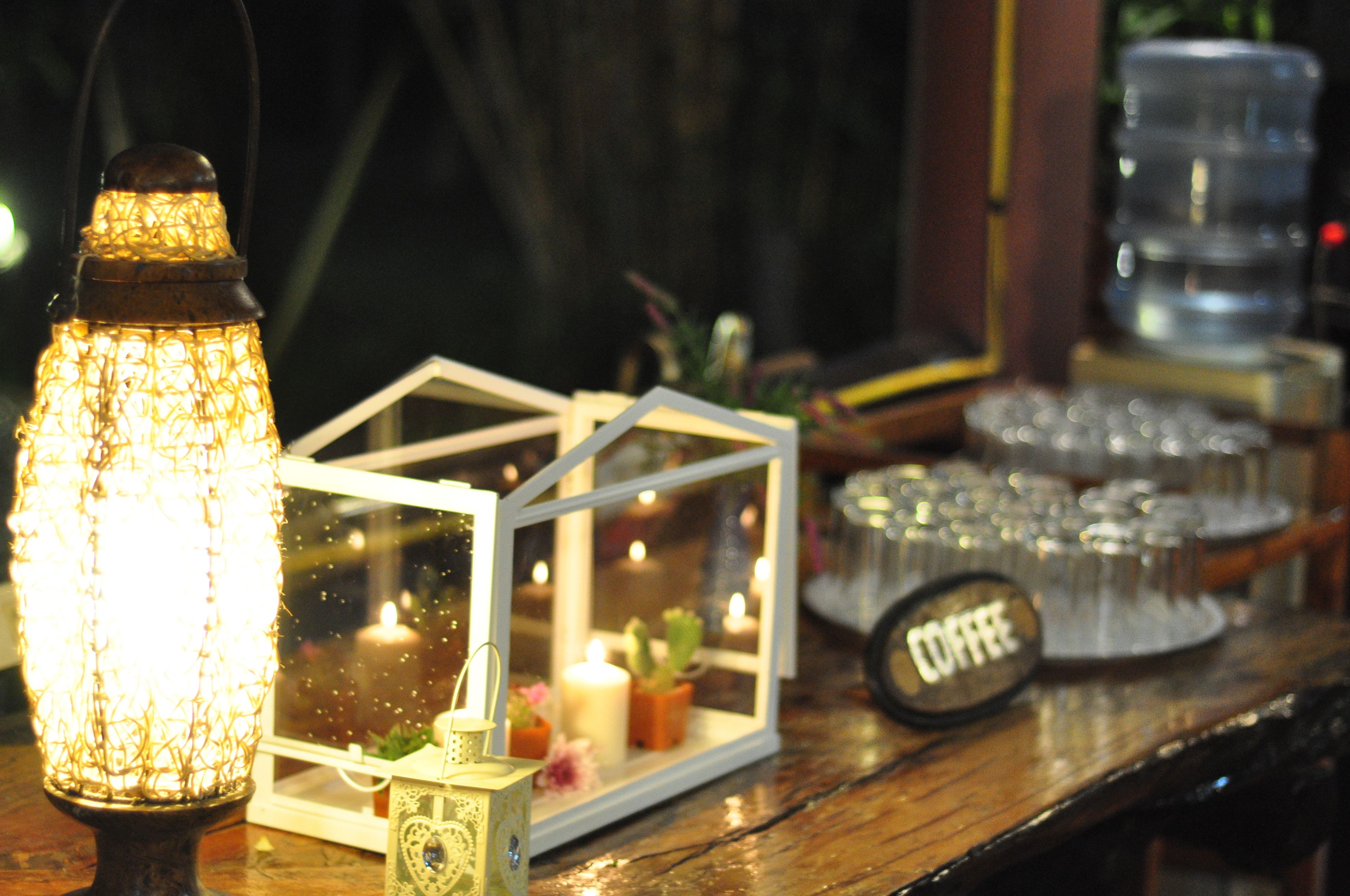 A table with a decorative lantern, a small glass house with candles, and a coffee station.