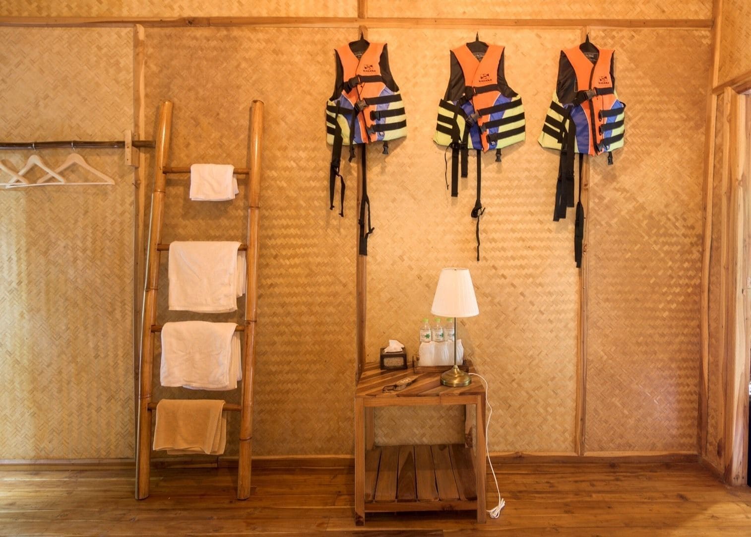 A room with a wooden floor, a wooden ladder, and three life jackets hanging on the wall.