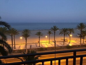 A beach view with palm trees and street lights.