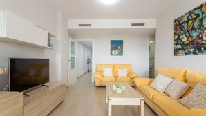 Un salon moderne avec un téléviseur à écran plat, un canapé jaune, une table basse et un tableau accroché au mur.