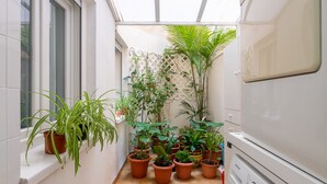 Un couloir étroit, bordé de plantes en pot le long des murs, avec une fenêtre sur la gauche et un lave-linge sur la droite.