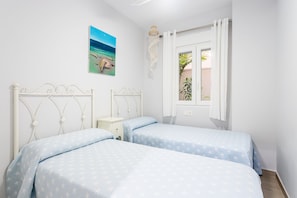 A bedroom with two beds, a nightstand, a window with curtains, and a painting on the wall.