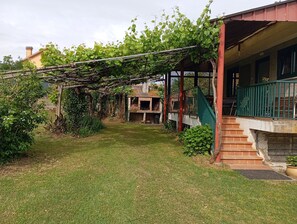 A backyard with a pergola, a brick oven, and a staircase leading to a porch.