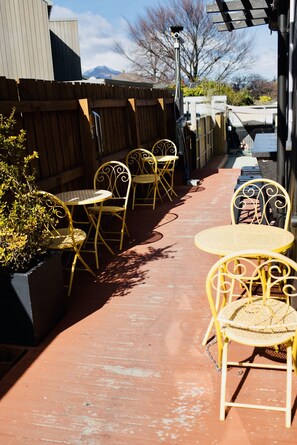 Une terrasse avec des chaises et des tables en métal jaune, une clôture en bois et une vue sur les montagnes en arrière-plan.