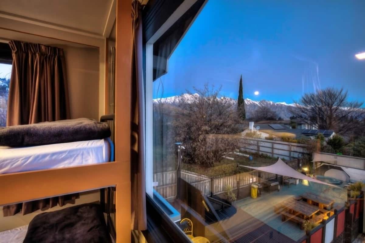 Una habitación con literas, un ventanal con vista a una montaña nevada y un jardín afuera.