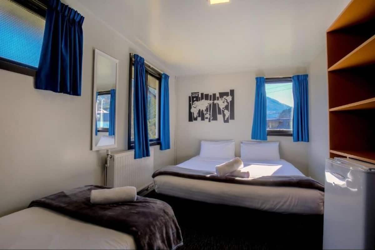 Habitación de hotel con dos camas, un mapa mundial en la pared y una ventana con cortinas.